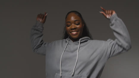 Studio-Portrait-Shot-Of-Young-Woman-Wearing-Hoodie-Dancing-With-Low-Key-Lighting-Against-Grey-Background-3